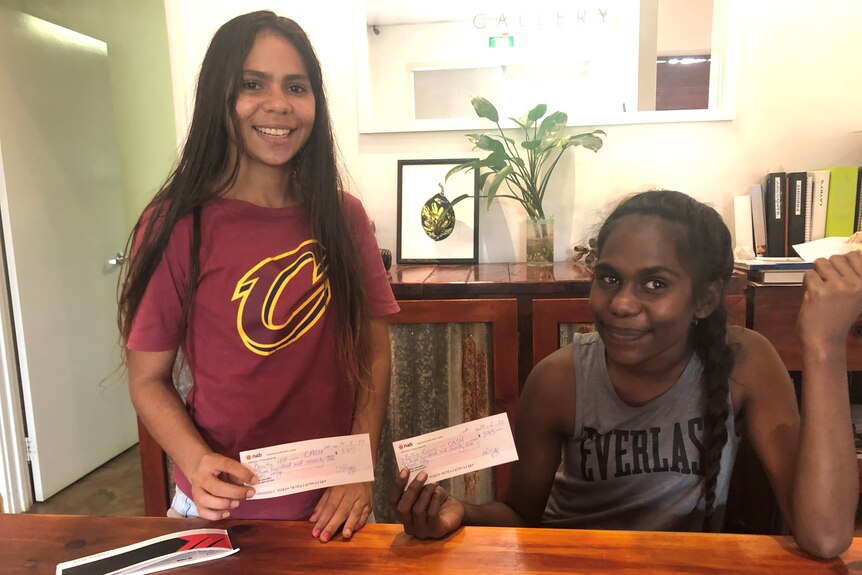 Two young indigenous girls holding up their first pay cheques.