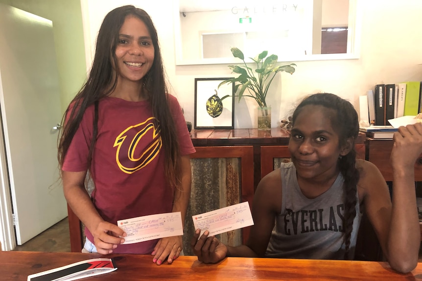 Two young indigenous girls holding up their first pay cheques.