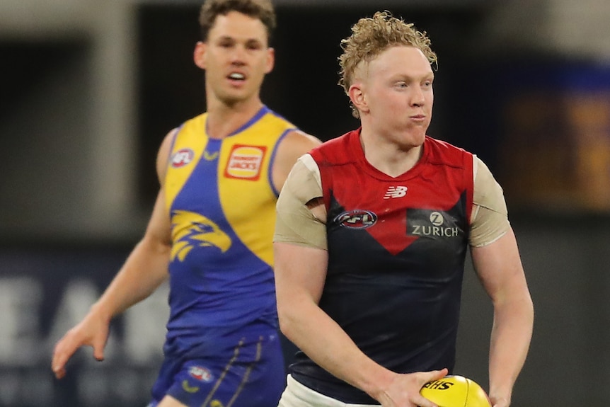 A Melbourne AFL midfielder looks down the field as he shapes to kick the ball during a match.