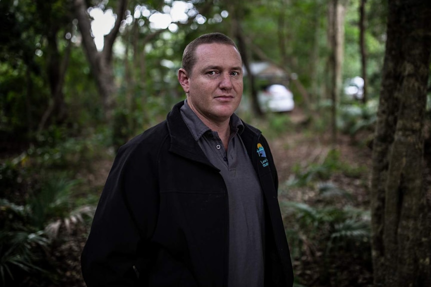 A man standing in a forest looks at the camera.