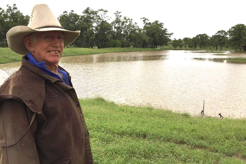 A farmer stands in front of a dam.