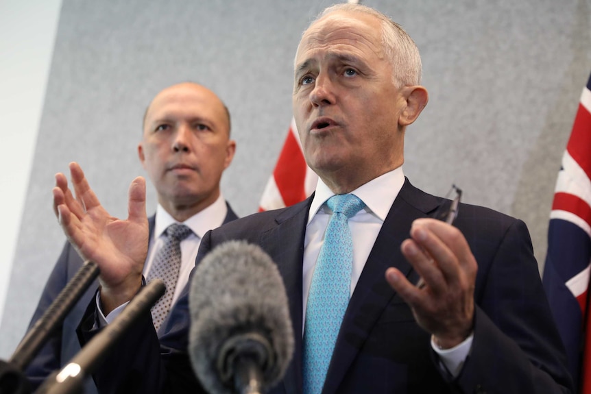 Malcolm Turnbull gestures at the microphone while Peter Dutton stares at him from behind.