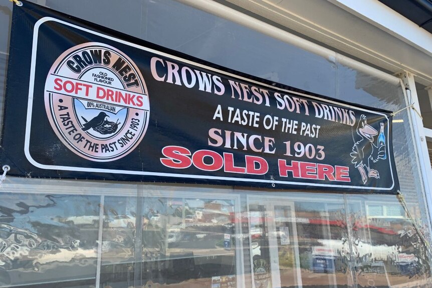 A black sign on a shop front reading 'Crows Nest Soft Drinks, a taste of the past since 1903'.