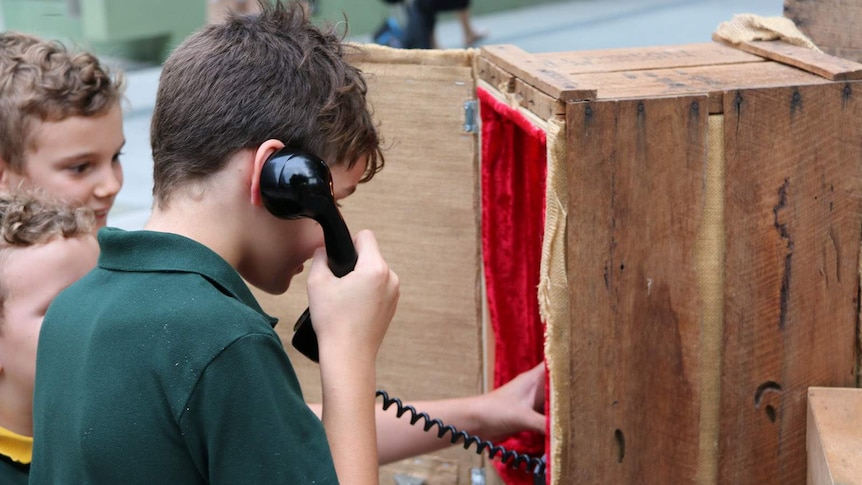 A boy holding the earpiece to an old bakelite phone