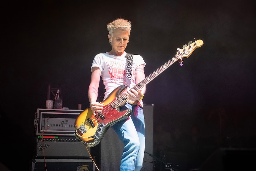 Vanessa Thornton of Jebediah plays her sunburst Fender bass on stage. She wears a white shirt and blue jeans.