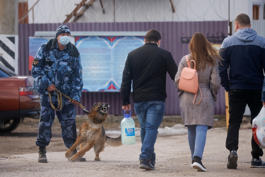 People walk past a Russian security guard with a dog.