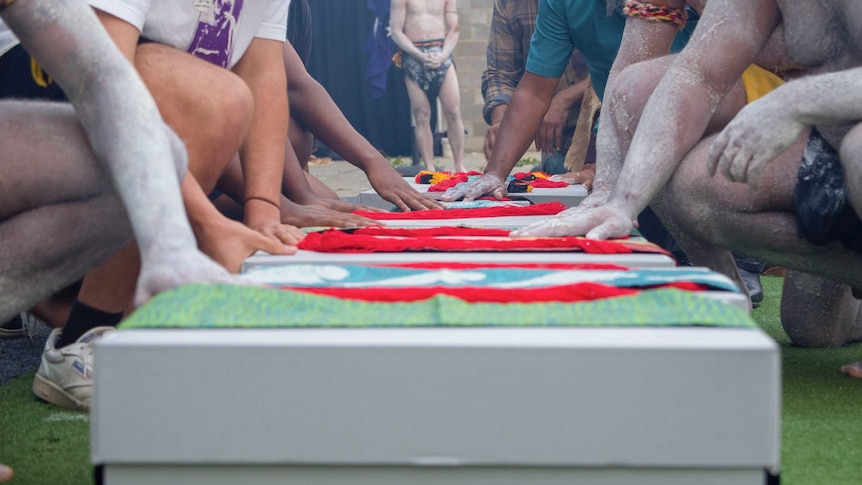 People placing their hands on the ancestral remains boxed for their return journey to Broome