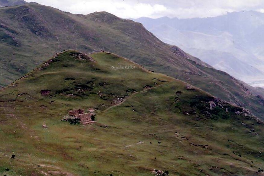 A small brick building sits on grass covered hills in Tibet