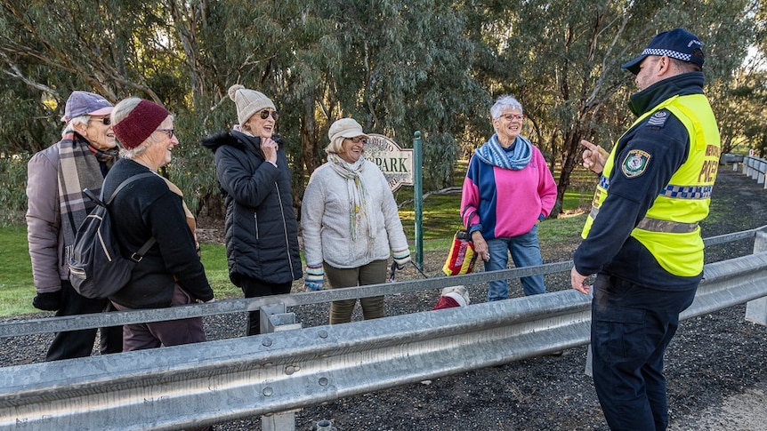 Several elderly women smile and laugh while speaking with a NSW police officer at a bridge checkpoint.