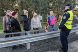 Several elderly women smile and laugh while speaking with a NSW police officer at a bridge checkpoint.