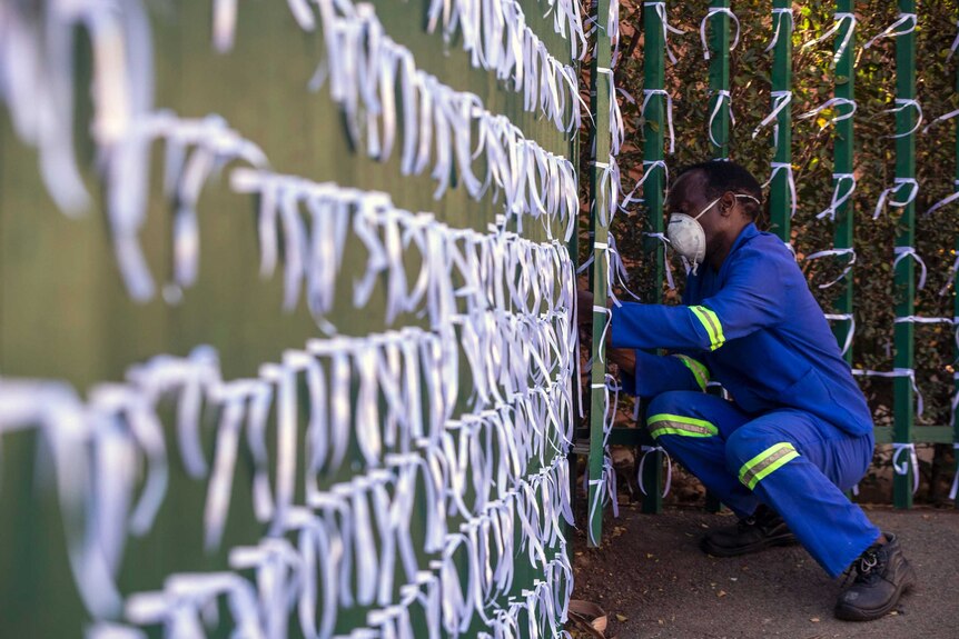 A man ties a ribbon onto a fence.