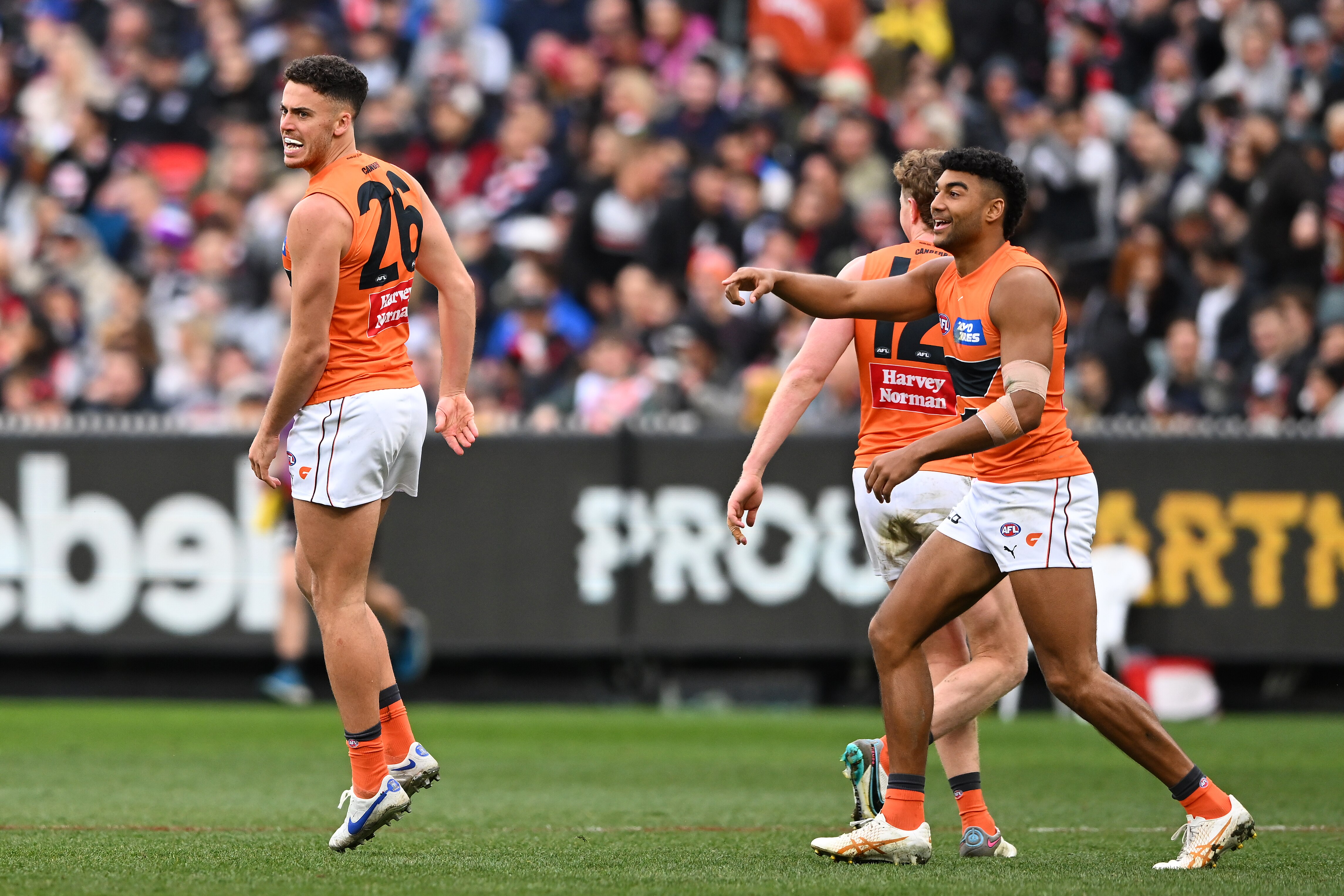 A Giants AFL player jumps in the air in celebration as a smiling teammate points at him after a goal.