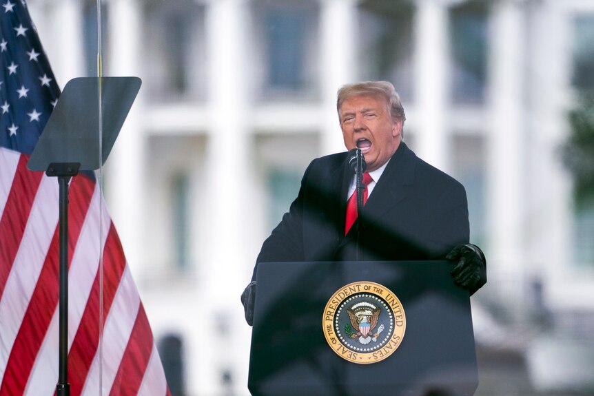 Donald Trump leans into the microphone as he speaks loudly behind a presidential lectern in front of the White House.