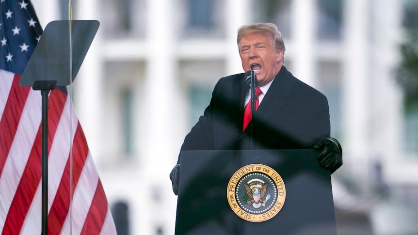 Donald Trump leans into the microphone as he speaks loudly behind a presidential lectern in front of the White House.