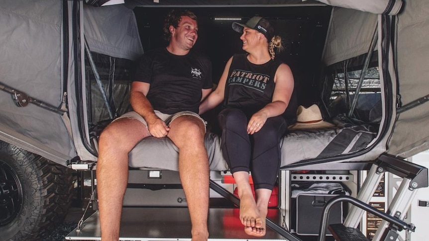 A man and woman sitting in the back of a caravan. 