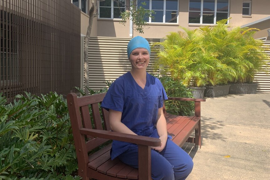 Georgia Stephens sitting on a bench outside in her navy blue hospital scrubs.
