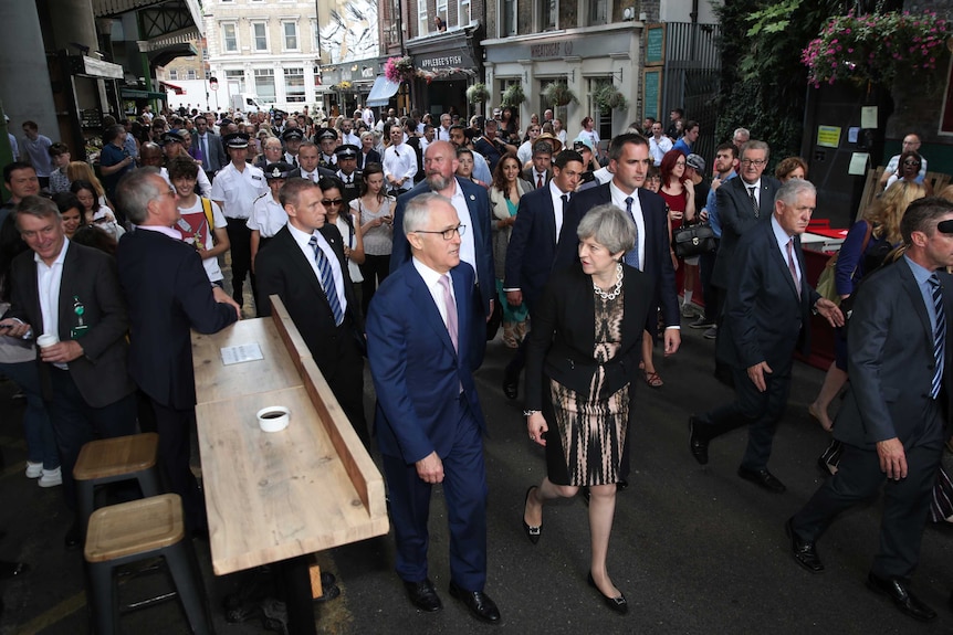 Malcolm Turnbull and Theresa May walk through a crowded Borough Market, followed by police.