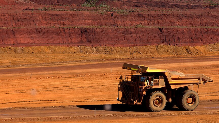 A large mining dump truck drives across red soil.