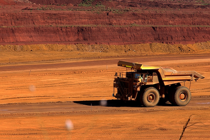 A large mining dump truck drives across red soil.