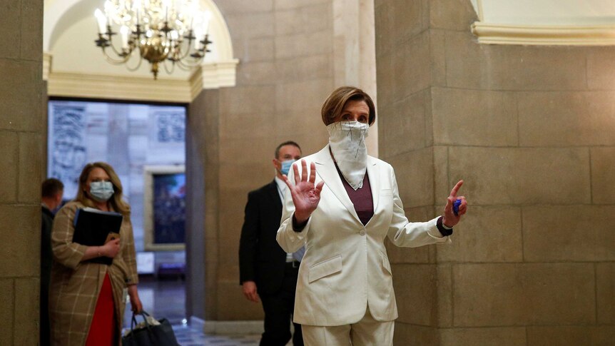 Nancy Pelosi walking to the House Chamber with a white bandana over her face, holding up 7 fingers.