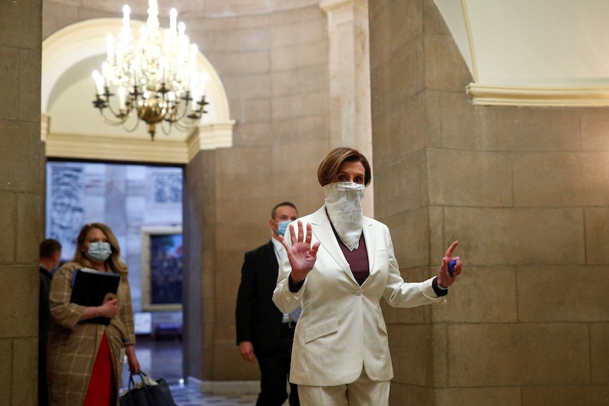 Nancy Pelosi walking to the House Chamber with a white bandana over her face, holding up 7 fingers.
