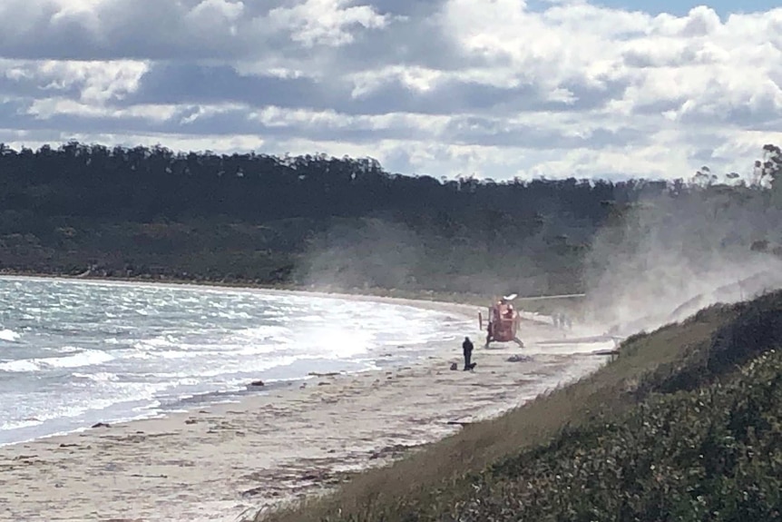 A helicopter lands on a beach.