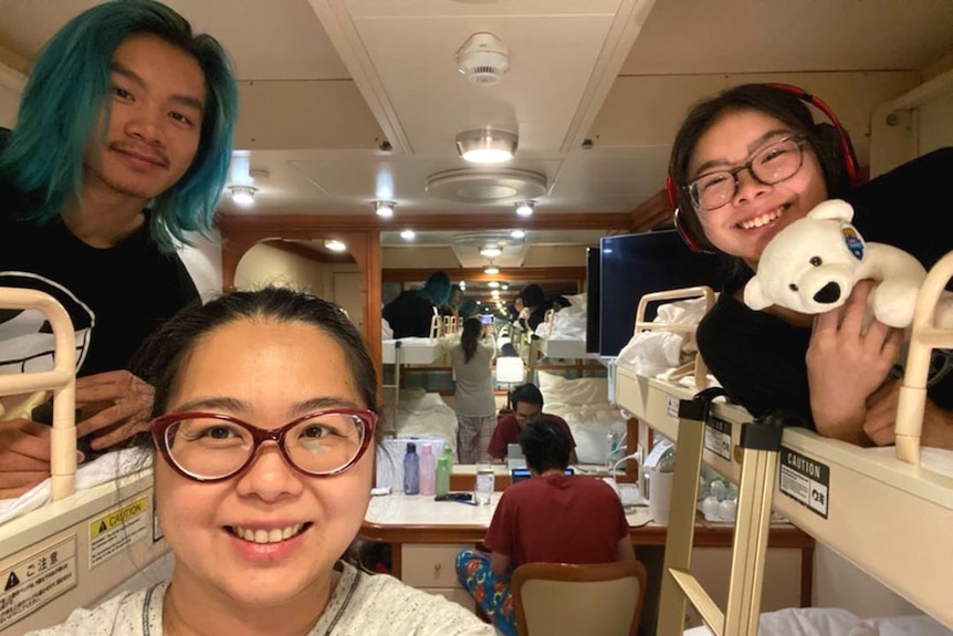 A family smiling at the camera inside a ship's cabin, a man facing away in the background