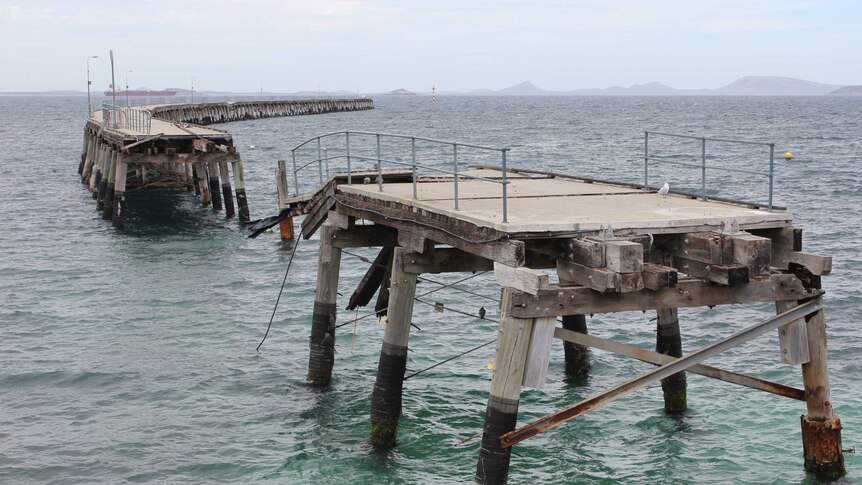 A long timber jetty stretching into the ocean, with parts that have crumbled into the water.