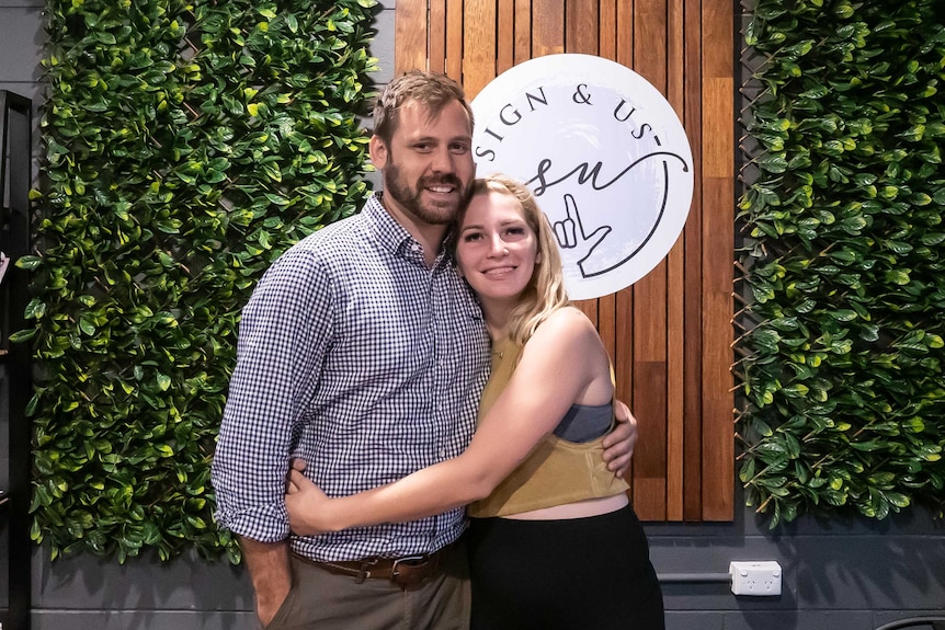 A couple embrace, smiling for a photo, inside of gym.