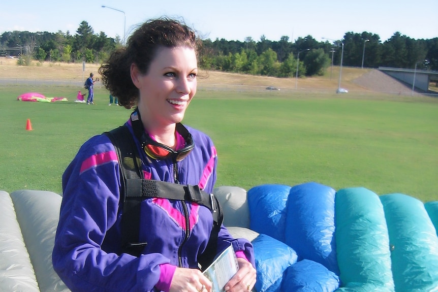 A parachute can be seen in the background as a woman who has just skydived smiles.