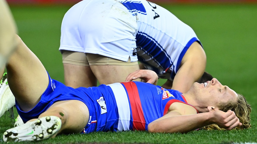 A Western Bulldogs AFL palyer lies on the ground concussed.