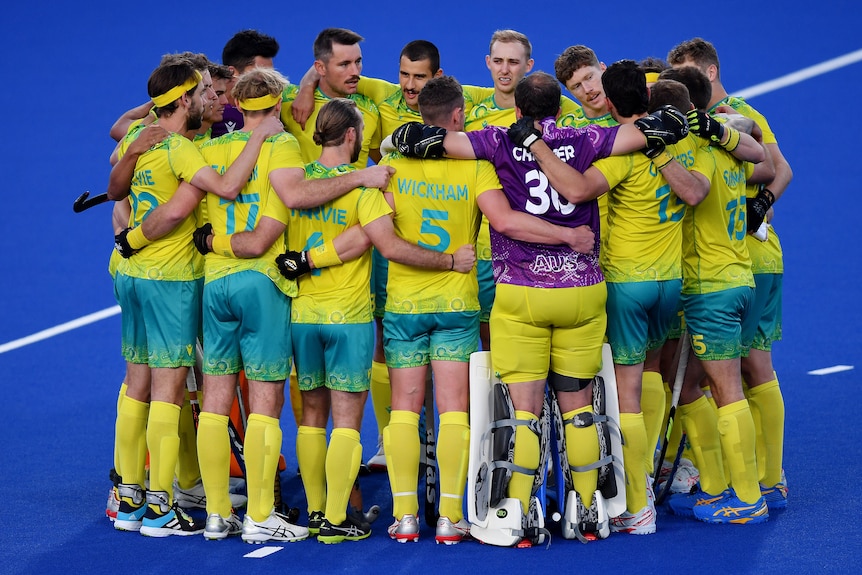 The Australian men's hockey squad gather in a tight circle with their arms around each others' shoulders.