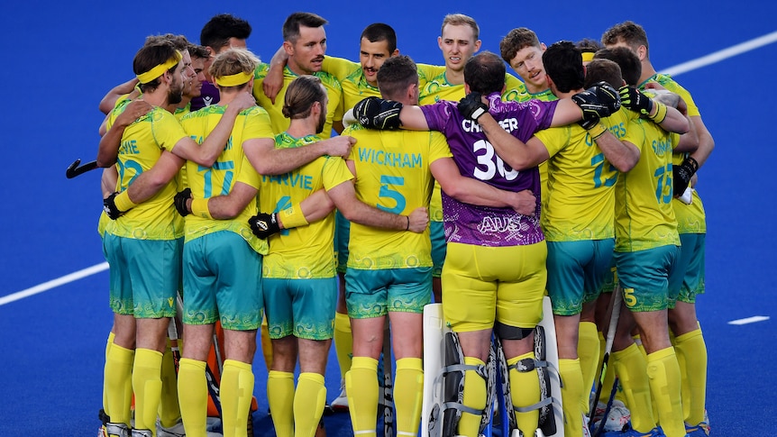 The Australian men's hockey squad gather in a tight circle with their arms around each others' shoulders.