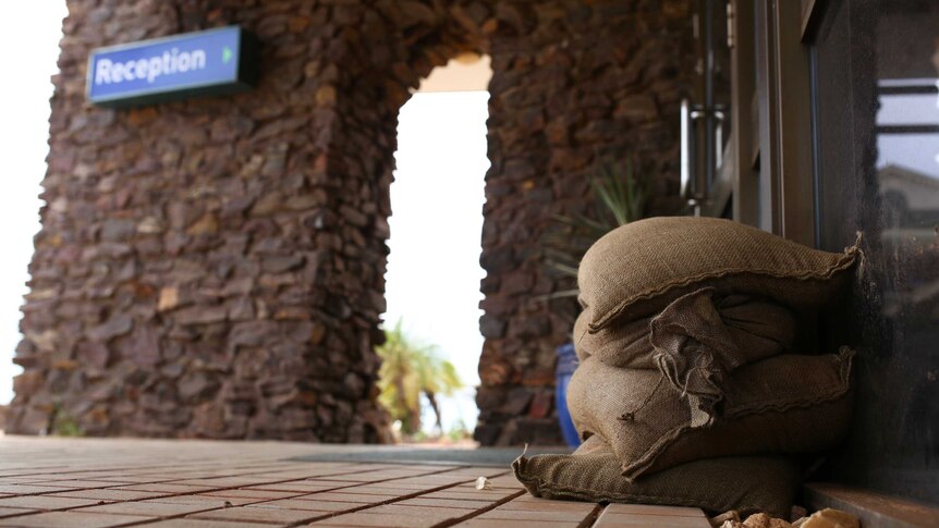 A close-up shot of sandbags on the ground at the entrance to a Port Hedland hotel with a blue reception sign in the background.