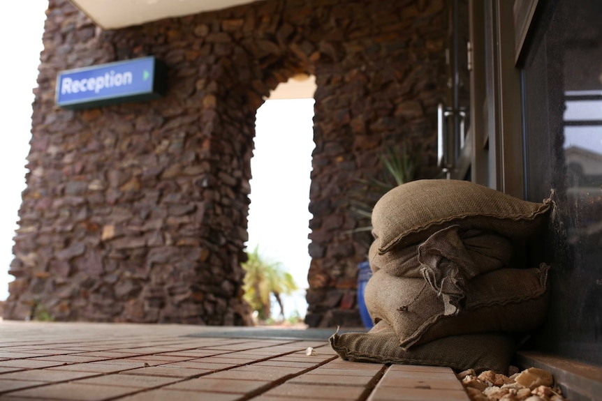 A close-up shot of sandbags on the ground at the entrance to a Port Hedland hotel with a blue reception sign in the background.