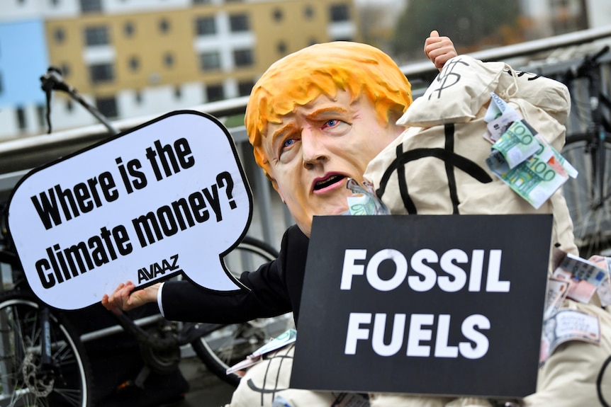 A person wearing a mask depicting Britain's Prime Minister Boris Johnson protests.