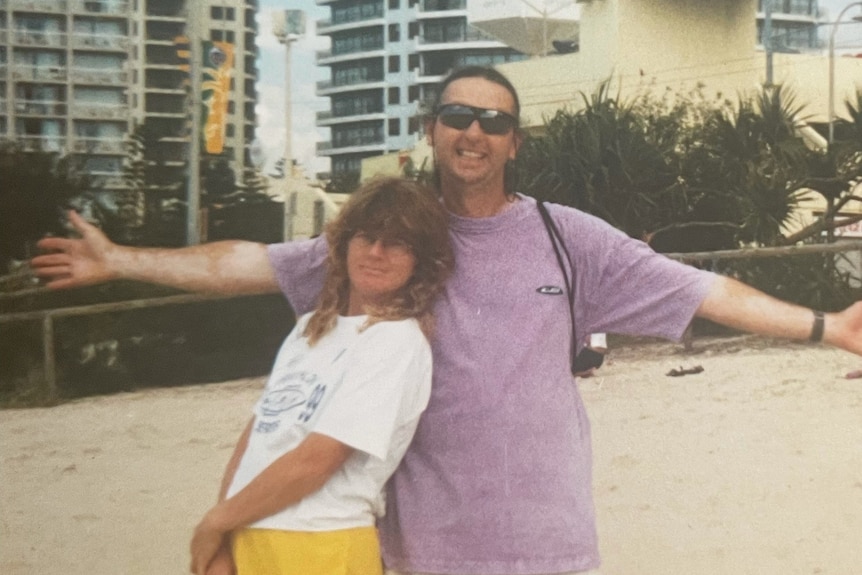 a woman in a white t-shirt pictures with a man with outstretched arms on a beach