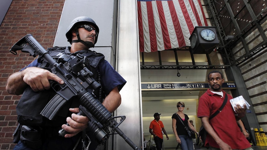 New Yorkers walk past a police officer holding a machine gun on a street in Lower Manhattan.