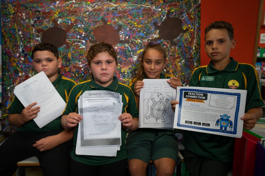 Four children holding up schoolwork pages.