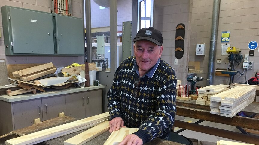 An 89-year-old man with an acquired brain injury sands a piece of timber in a workshop