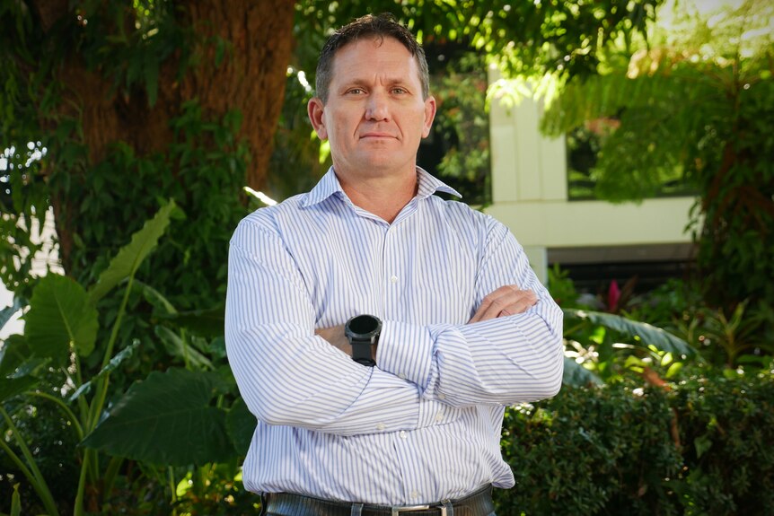 Townsville deputy mayor Mark Molachino stands with his arms crossed in front of a garden