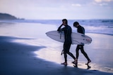 Two men walk along the beach carring their surfboards
