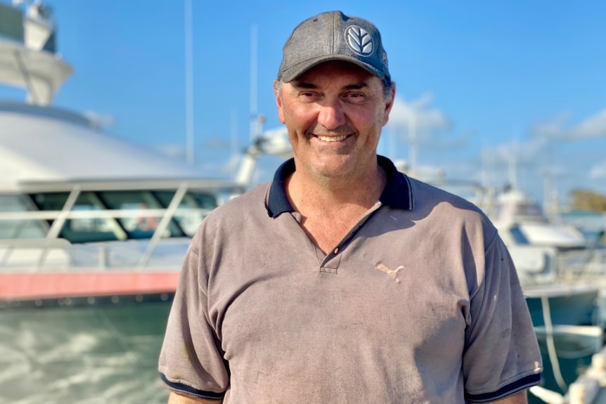 Man in cap and polo shirt smiling, in front of a boat