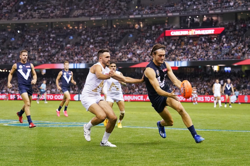 An AFL player in a charity match gets ready to kick the ball as his opponent tries to grab him.