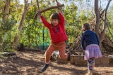 A girl in red hangs off a home-made swing, as two other children play nearby.