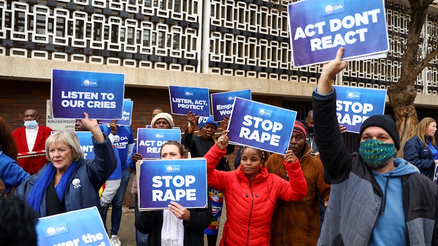 A group of protesters are pictured carrying placards with texts like 'listen to our cries', 'act dont react' and 'stop rape' 