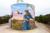 Artists work on a giant mural on a silo in a country town.