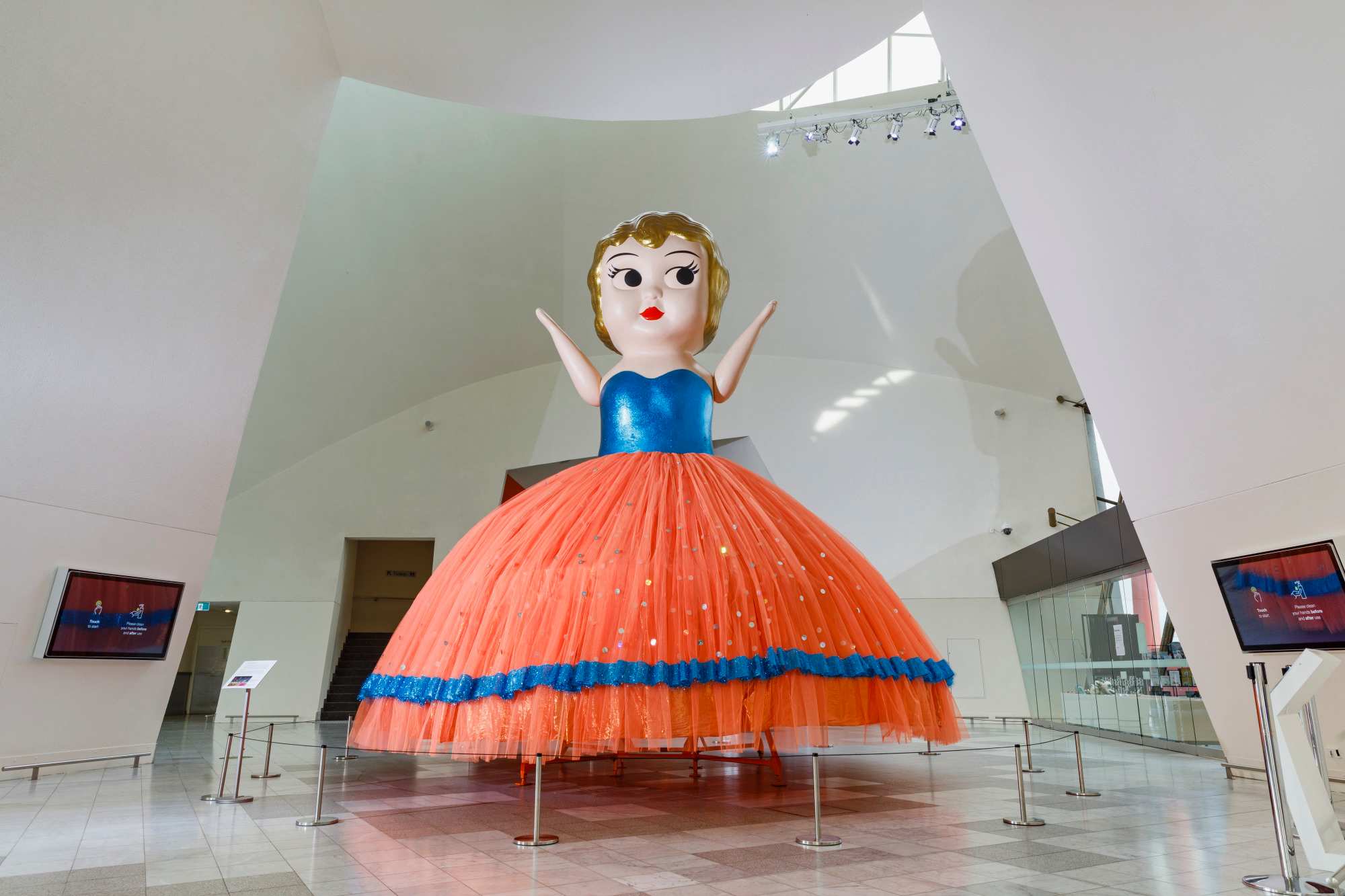 Boneca Kewpie gigante com blusa azul e saia laranja no foyer do Museu Nacional da Austrália
