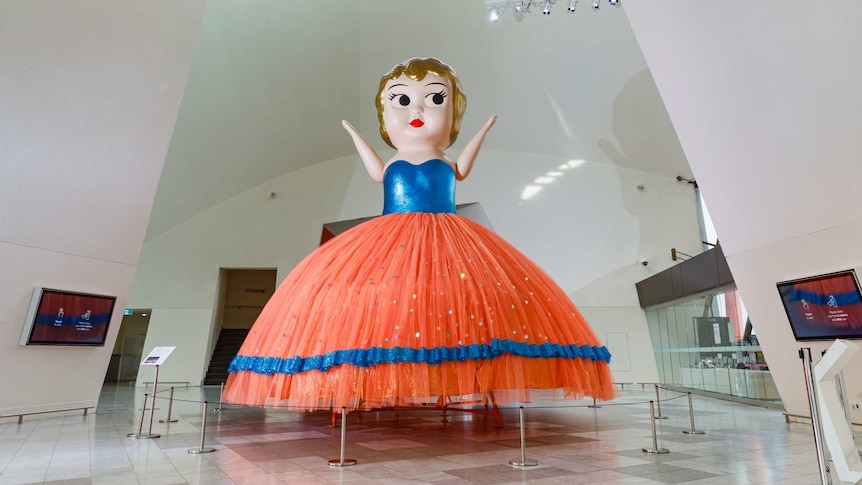 Giant kewpie doll in blue top and orange skirt in the foyer of the National Museum of Australia