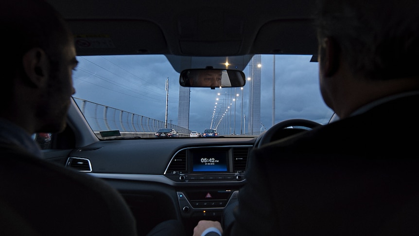 Two men sit in the front of a car driving on the freeway in Melbourne 